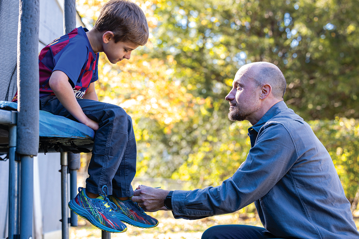 A man ties a boy’s shoe.